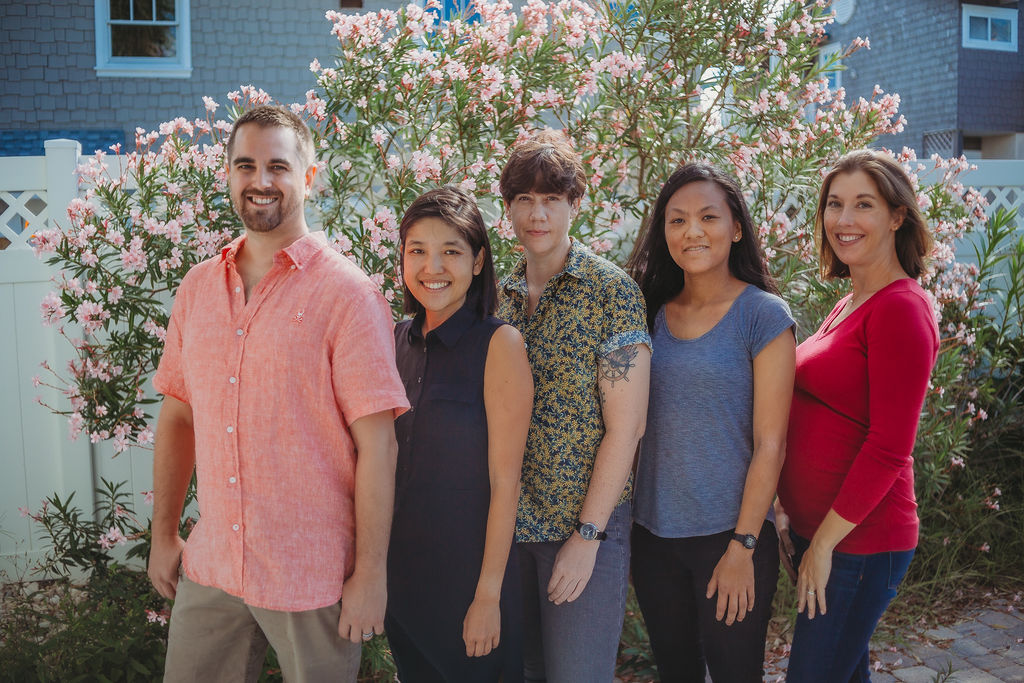 The first 5 Compiler Employees stand side-by-side in front of a garden of pink flowers